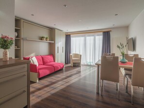 A modern hotel room with a sofa, dining table, chairs, a TV, and a window with curtains. - Alpen Leukerbad # 2-bed apartment, Dusche, WC by Interhome (Leukerbad)