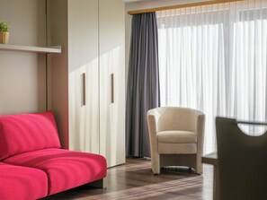 A room with a red sofa, a beige armchair, and a wooden shelf with a plant. - Alpen Leukerbad # 2-bed apartment, Dusche, WC by Interhome (Leukerbad)