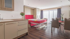 Hotellihuone, jossa on sänky, työpöytä, tuoli, pieni pöytä, maljakko kukkineen ja ikkuna, jossa on verhot.