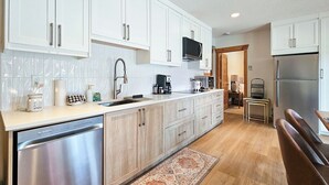 A modern kitchen with white cabinets, stainless steel appliances, and a wooden dining area. - Log Style Home with Hot Tub on the Golf Course! (Radium Hot Springs)