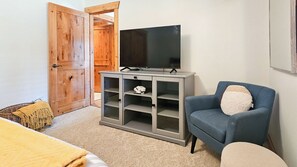 A room with a wooden door, a grey cabinet with shelves, a blue armchair, and a television on top. - Log Style Home with Hot Tub on the Golf Course! (Radium Hot Springs)