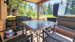 An outdoor patio with a grill, table, chairs, and a propane tank. - Log Style Home with Hot Tub on the Golf Course! (Radium Hot Springs)