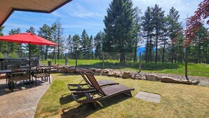 A patio with outdoor furniture, a grill, and a view of a forested area. - Log Style Home with Hot Tub on the Golf Course! (Radium Hot Springs)