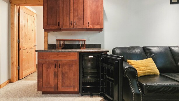 A compact kitchen with wooden cabinets, a built-in oven, and a black refrigerator. - Log Style Home with Hot Tub on the Golf Course! (Radium Hot Springs)