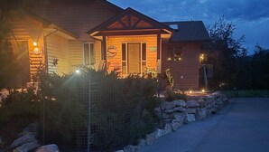 A two-story log cabin with a stone foundation, a porch with a railing, and a visible garage door. - Log Style Home with Hot Tub on the Golf Course! (Radium Hot Springs)