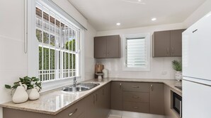 A kitchen with a sink, countertop, cabinets, and a refrigerator. - Coastal Corner Poolside Retreat on The Strand (North Ward)