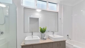 A modern bathroom with two sinks, a large mirror, and a shower area. - Coastal Corner Poolside Retreat on The Strand (North Ward)