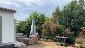 Un patio con mobiliario exterior, una parrilla y abundante vegetación.