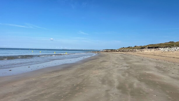 Una playa con cielo despejado, agua tranquila y una orilla arenosa.