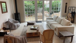 Un salón con sofá, sillón, mesa de centro, chimenea y vistas amplias a un patio exterior a través de puertas correderas de vidrio.