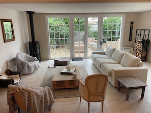 Ein Wohnzimmer mit einer Couch, einem Sessel, einem Couchtisch, einem Kamin und Blick durch große Schiebetüren auf eine Terrasse.