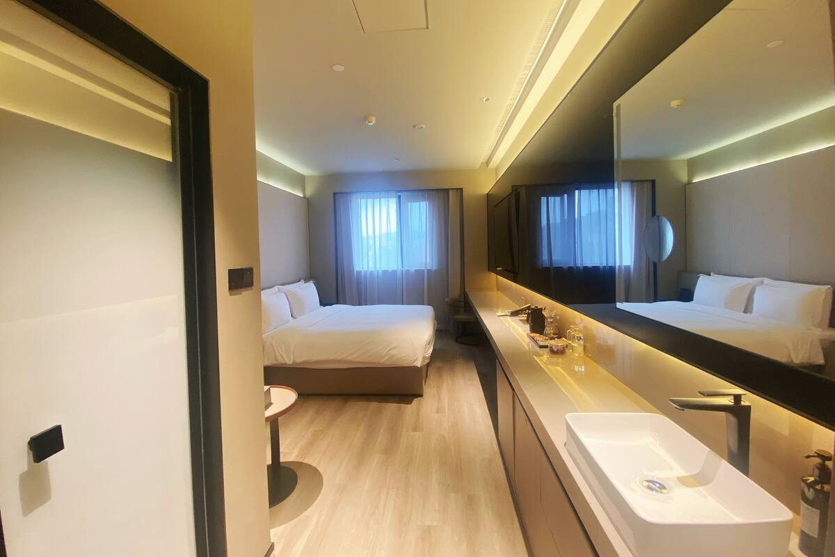 Ein Hotelzimmer mit Bett, einem großen Spiegel, einem Badezimmer mit Waschbecken und einem Fenster mit Vorhängen.