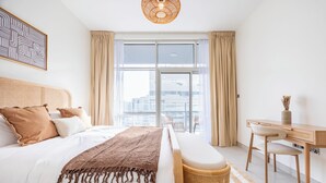 A modern hotel room with a large bed, a desk, and a view of the city. - Bloomfields 2BR in Lamar Raha Beach (Abu Dhabi)