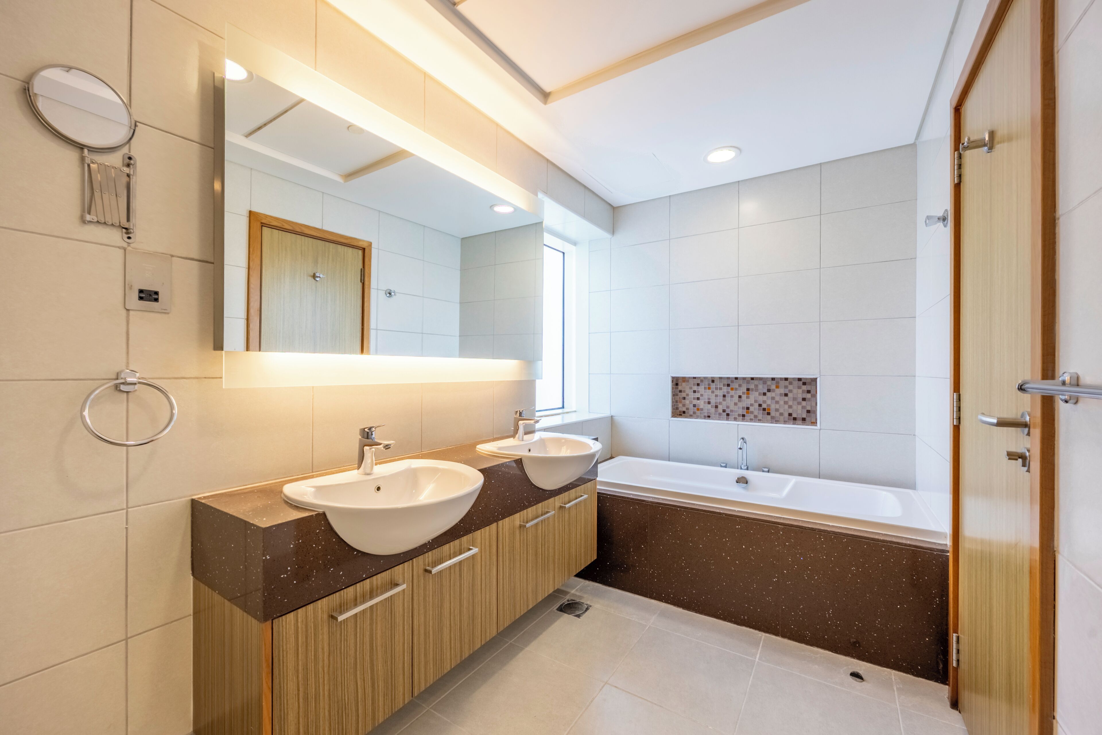 A modern bathroom with two sinks, a large mirror, and a bathtub.
