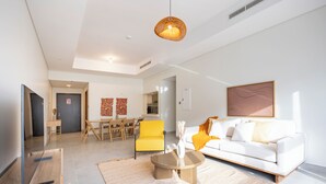 A modern living room with a white sofa, yellow armchair, and a coffee table. There is a dining area with a table and chairs in the background. - Bloomfields 2BR in Lamar Raha Beach (Abu Dhabi)