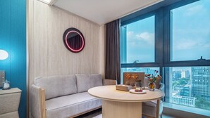 Una habitación moderna con sofá, una mesa redonda, un jarrón decorativo y vistas de la ciudad a través de grandes ventanales.