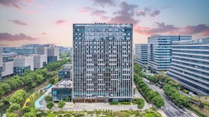 Un moderno edificio de gran altura con fachada enrejada, rodeado de vegetación y otras construcciones contemporáneas.