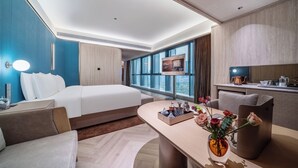 Una habitación de hotel moderna con una cama grande, un escritorio con un florero, un comedor y vistas de la ciudad.