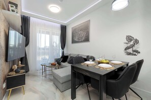 A modern living room with a flat-screen TV, a dining table set for four, and a sofa. - Stylish Apartment with Parking | Balcony | Air Conditioning | By the River (Szczecin)