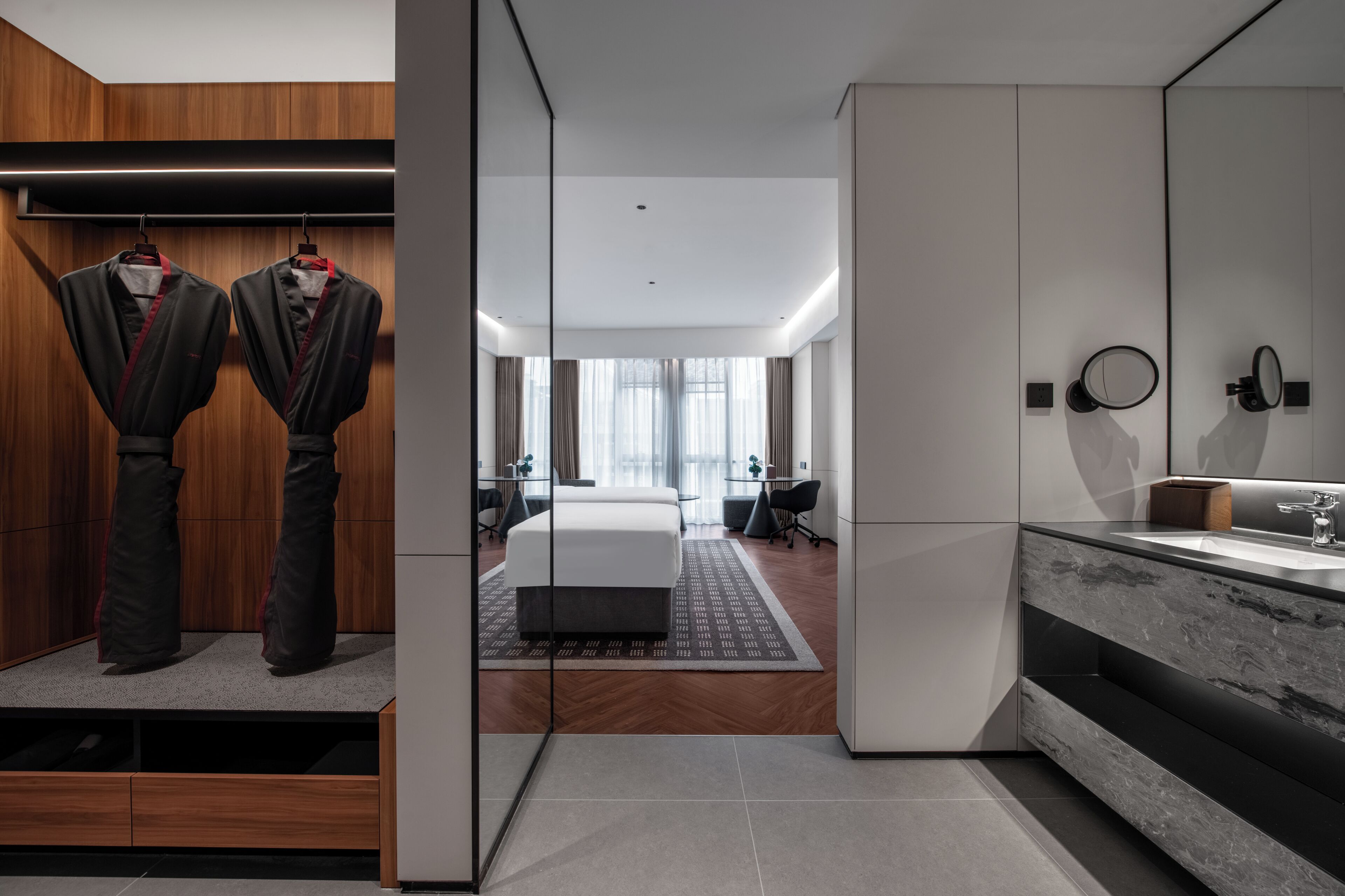 A modern hotel room with a bed, a bathroom with a mirror and sink, and a wardrobe with clothes.