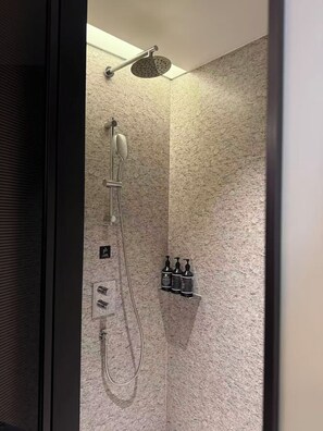 A shower with a handheld showerhead, a wall-mounted showerhead, and a handheld rain showerhead. There are three bottles of shampoo and conditioner on a shelf. - IntercityHotel Hangzhou Yuhang Xianlin (Hangzhou)