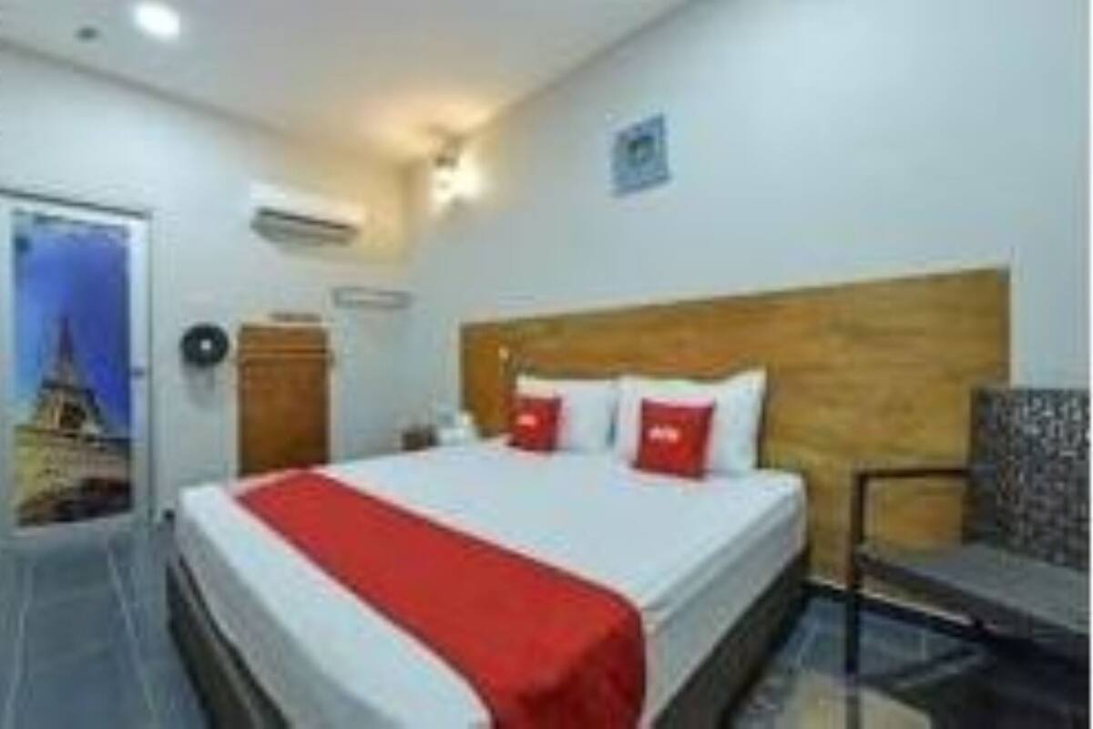 Hotellihuone, jossa on sänky, tuoli, seinään asennettu ilmastointilaite ja juliste seinällä.