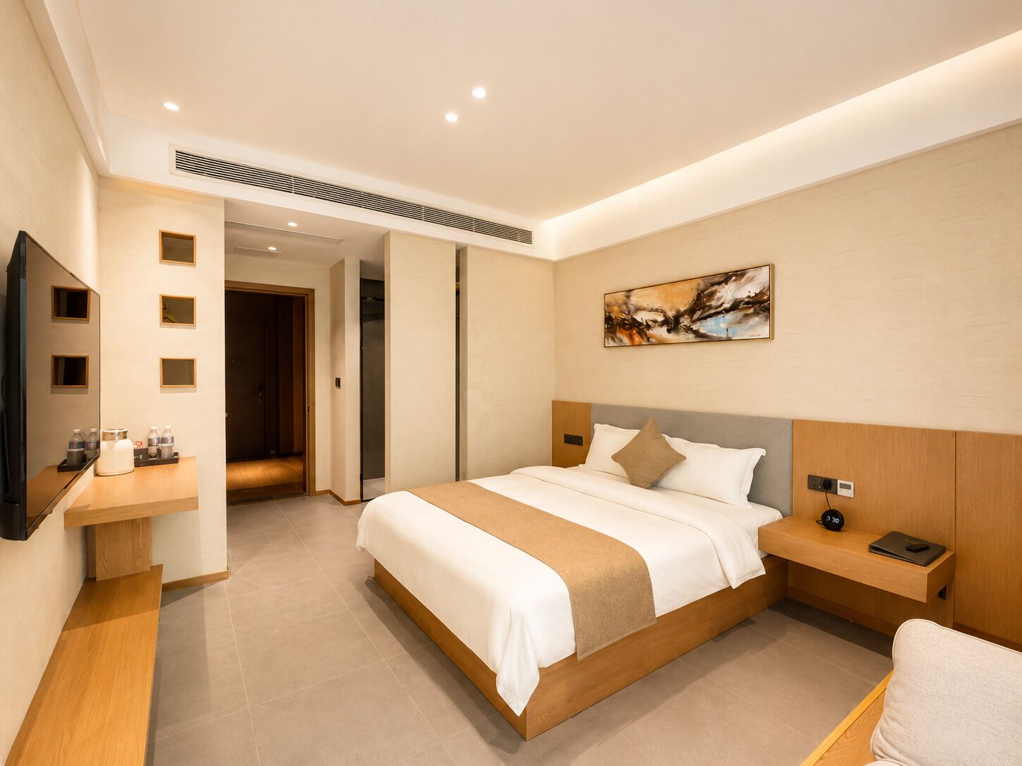 Quarto de hotel com cama, mesa de cabeceira, televisão, obras de arte e porta para outro quarto.