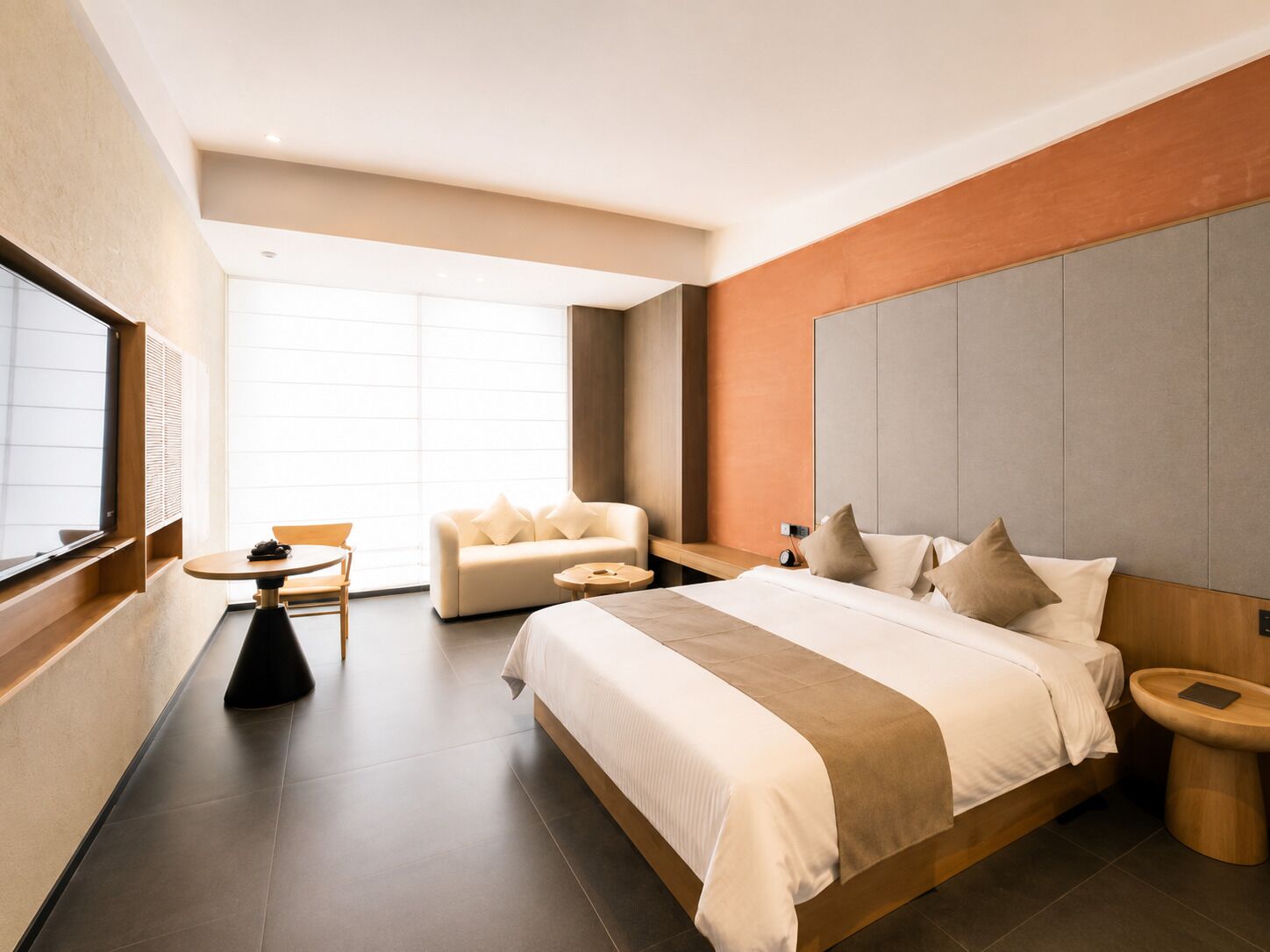 Una habitación de hotel moderna con una cama grande, un sofá, una mesita redonda y un televisor.