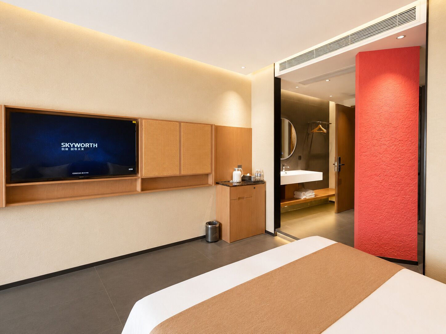 Et moderne hotelværelse med et stort fladskærms-tv, træskabe, en seng, et badeværelse med spejl og vask, samt en rød accentvæg.