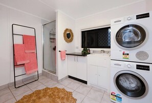 A laundry room with a washing machine, dryer, and a rack with pink towels. - Tropical Poolside Studio (Mundingburra)