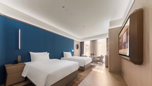 A hotel room with two beds, a TV, a desk, and a bathroom.