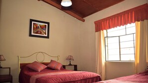 A bedroom with a bed, bedside tables, a lamp, a window with curtains, and a framed picture on the wall.