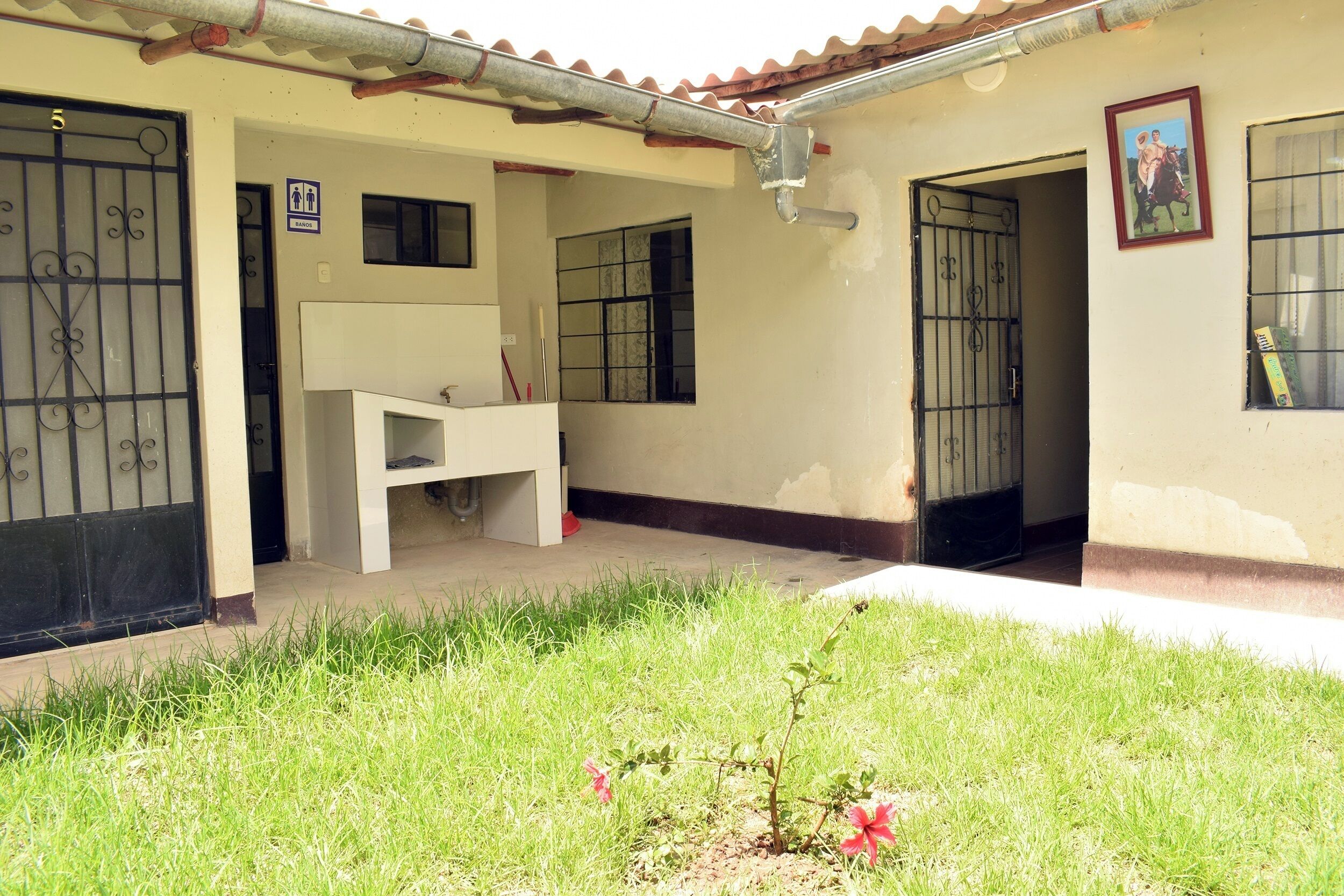 A building with a tiled roof, a white exterior, and a small garden area with grass and a pink flower.