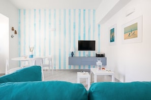 Ein modernes Wohnzimmer mit einer gestreiften Wand, einem Flachbildfernseher, einem kleinen Esstisch und sitzmöbeln in Türkis.