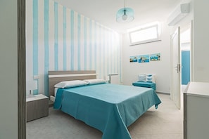 Ein Schlafzimmer mit Bett, Nachttischen, Fenster und einer Wand-Klimaanlage.
