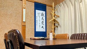 A conference room with a wooden table, leather chairs, a blue banner with Japanese text, and a wooden decorative piece.