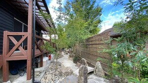 A narrow outdoor pathway flanked by wooden structures, with a wheelbarrow and a metal pole visible.