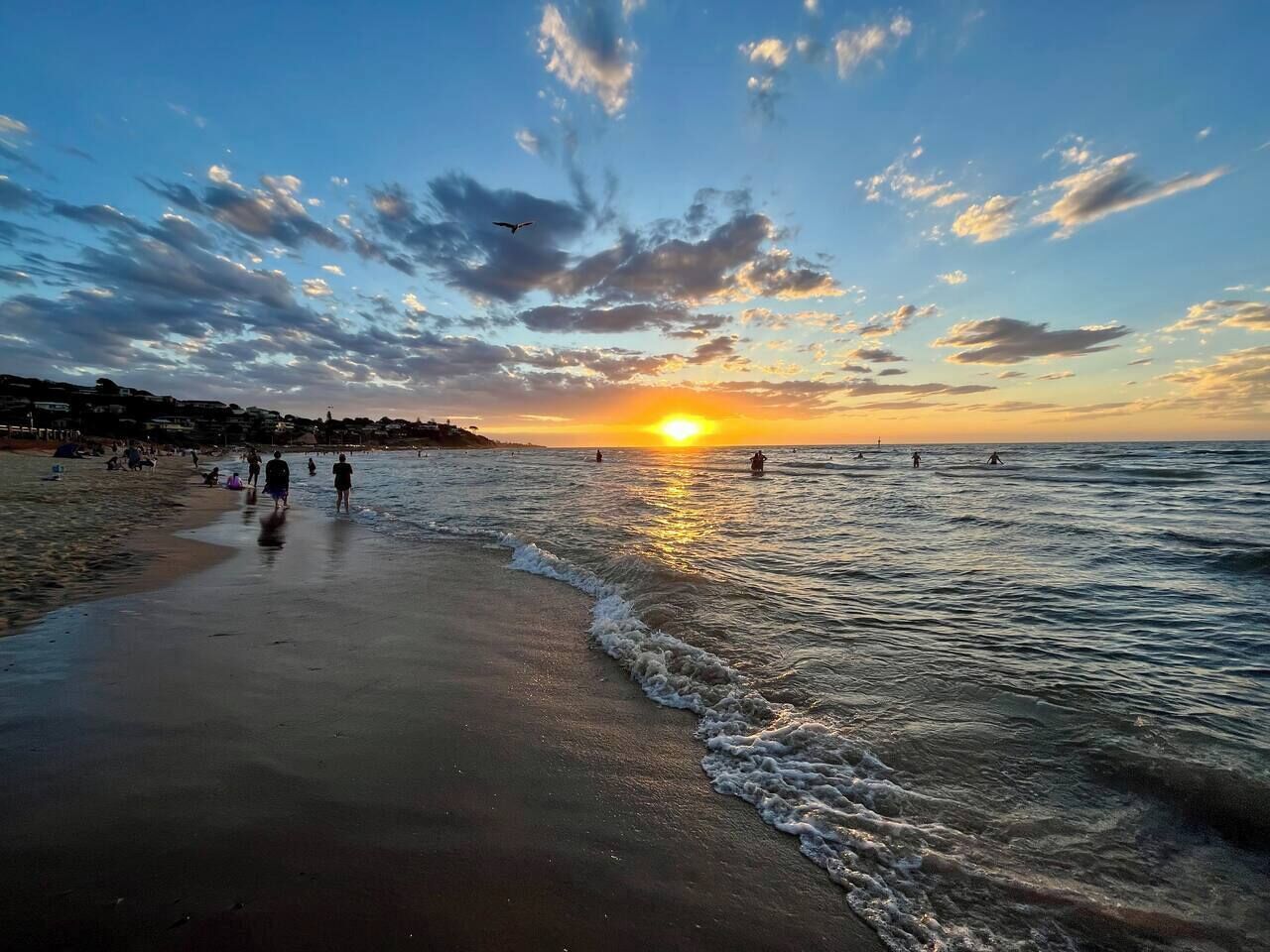 Una spiaggia con un tramonto, onde e persone che passeggiano.