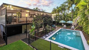 Una casa moderna de dos pisos amb piscina, un porxo cobert i vegetació tropical exuberant.