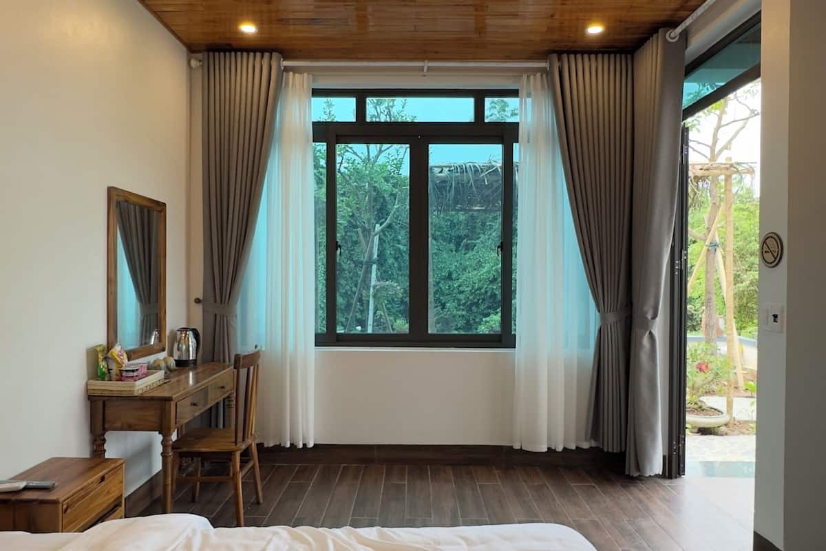 Un dormitorio con techo de madera, una cama grande, un escritorio con espejo y una ventana con cortinas.