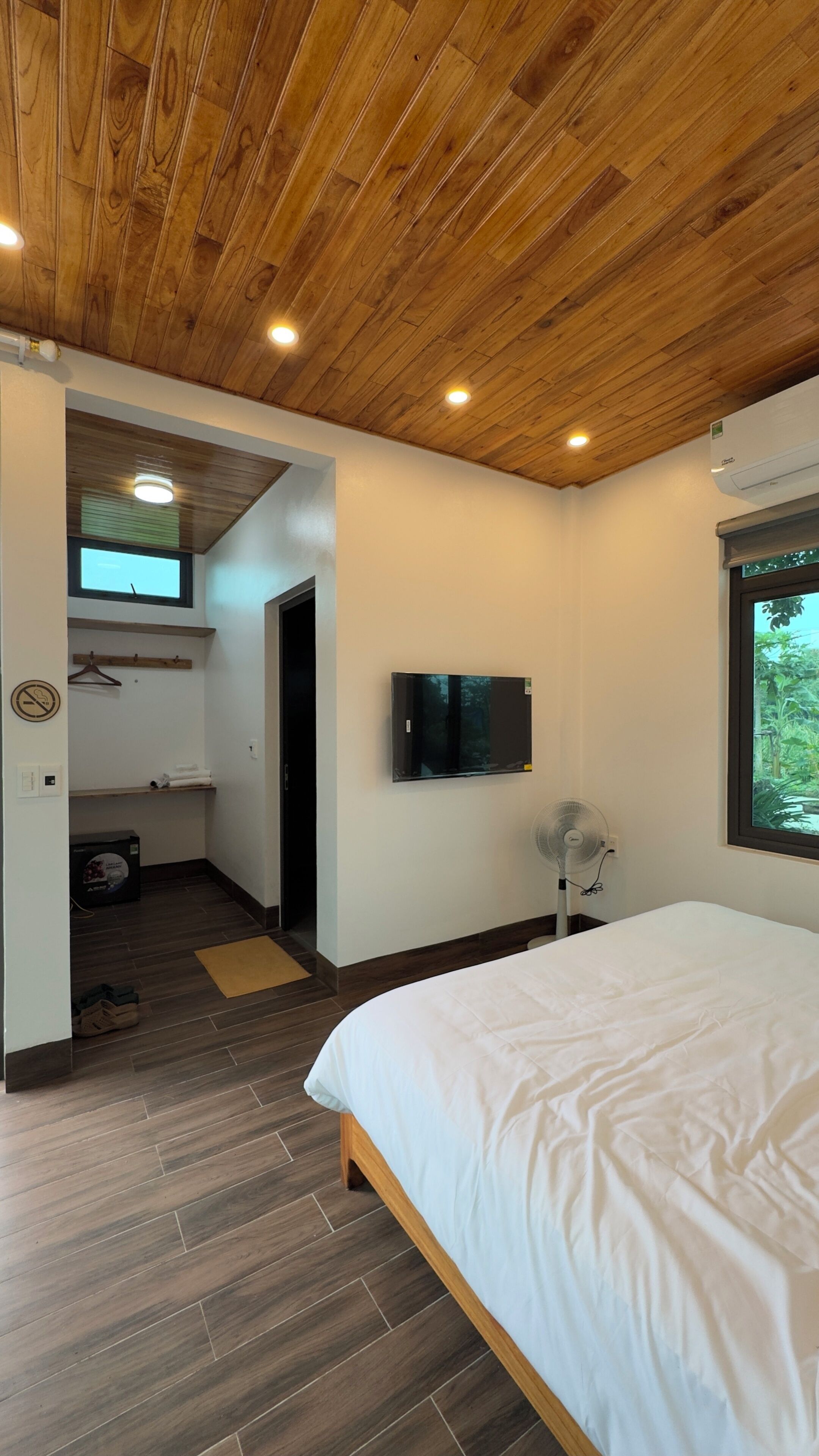 Une chambre avec un plafond en bois, un lit, une télévision et une fenêtre donnant sur un paysage verdoyant.