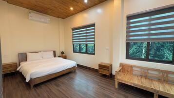 A bedroom with a wooden bed, a bench, a nightstand, and two windows with blinds.