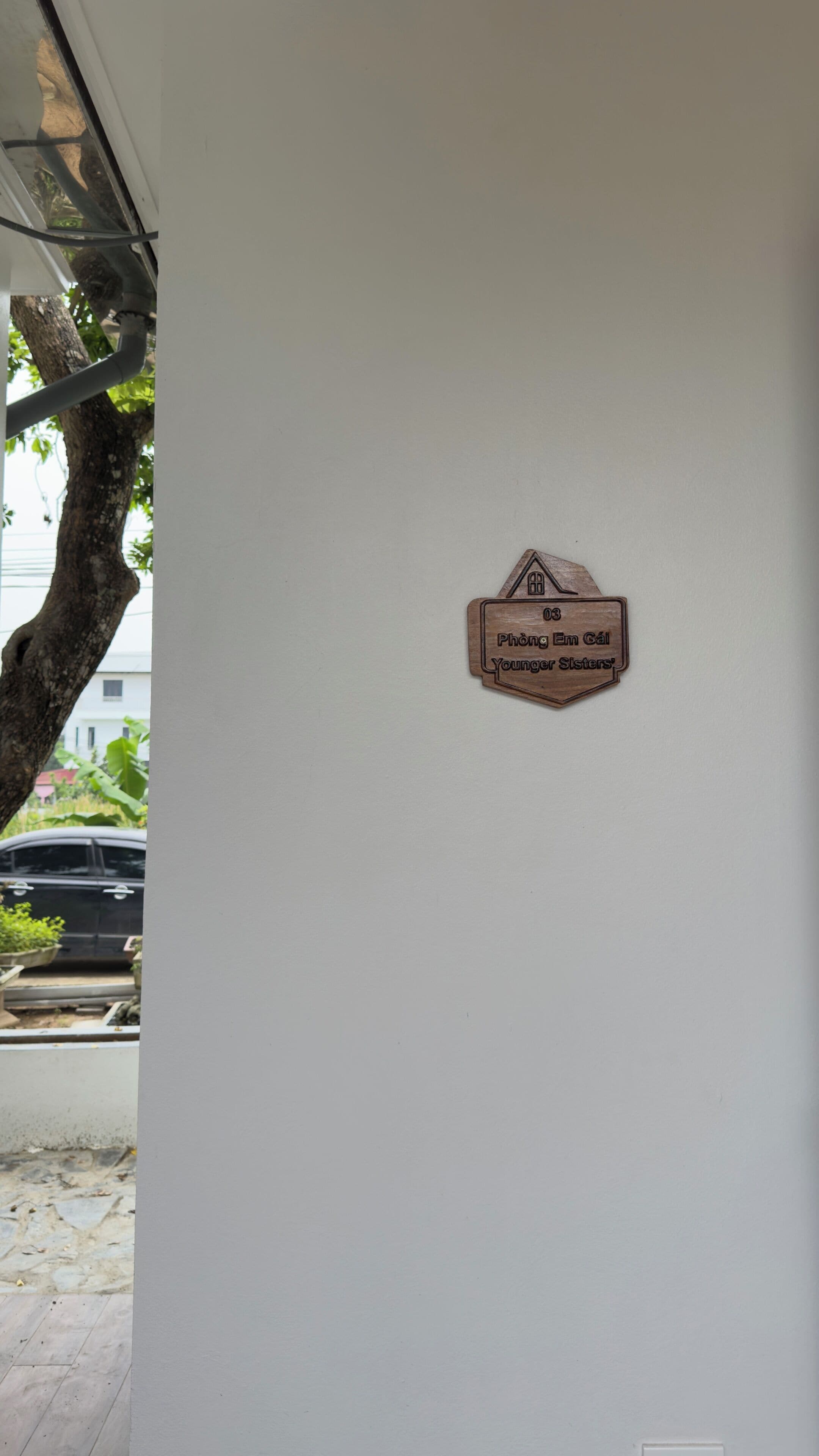 Een bord aan de muur met een icoontje van een huis en de tekst 'Phòng Em Gà Younger Sisters'.