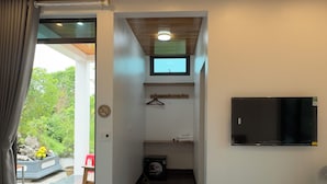 A bedroom with a wooden ceiling, a bed, a TV, and a small bathroom with a window.