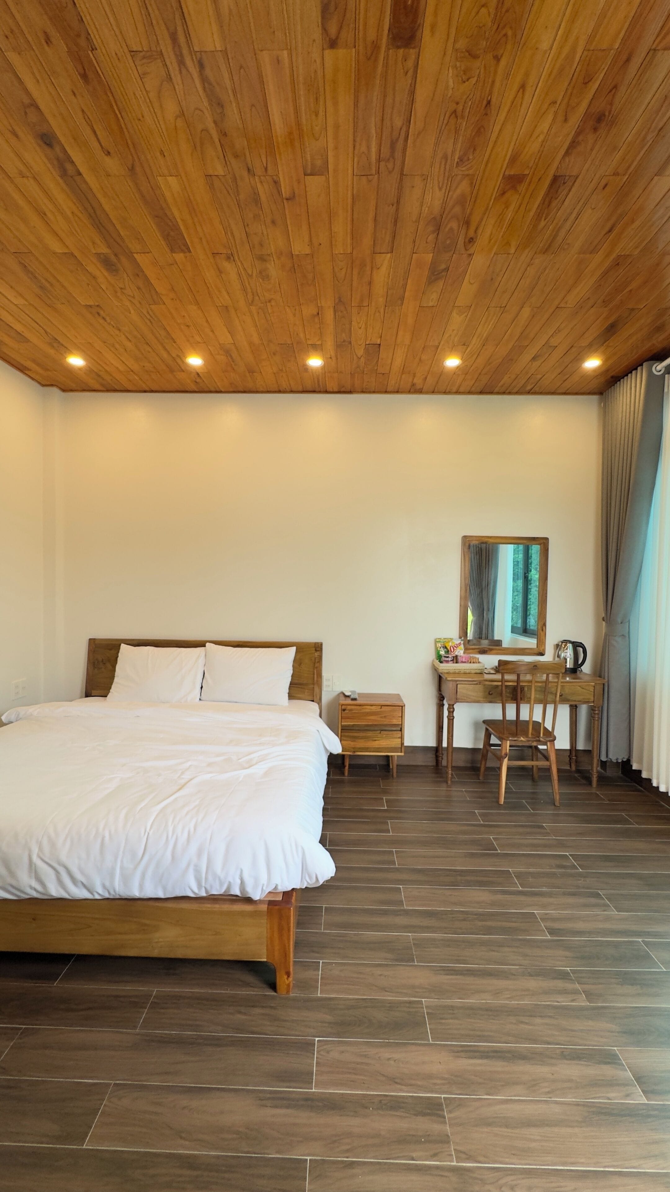 Um quarto com uma cama de madeira, uma escrivaninha com cadeira e um espelho.