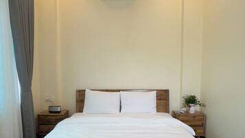 A bedroom with a wooden ceiling, a bed with white bedding, a nightstand with a lamp, and an air conditioning unit on the wall.
