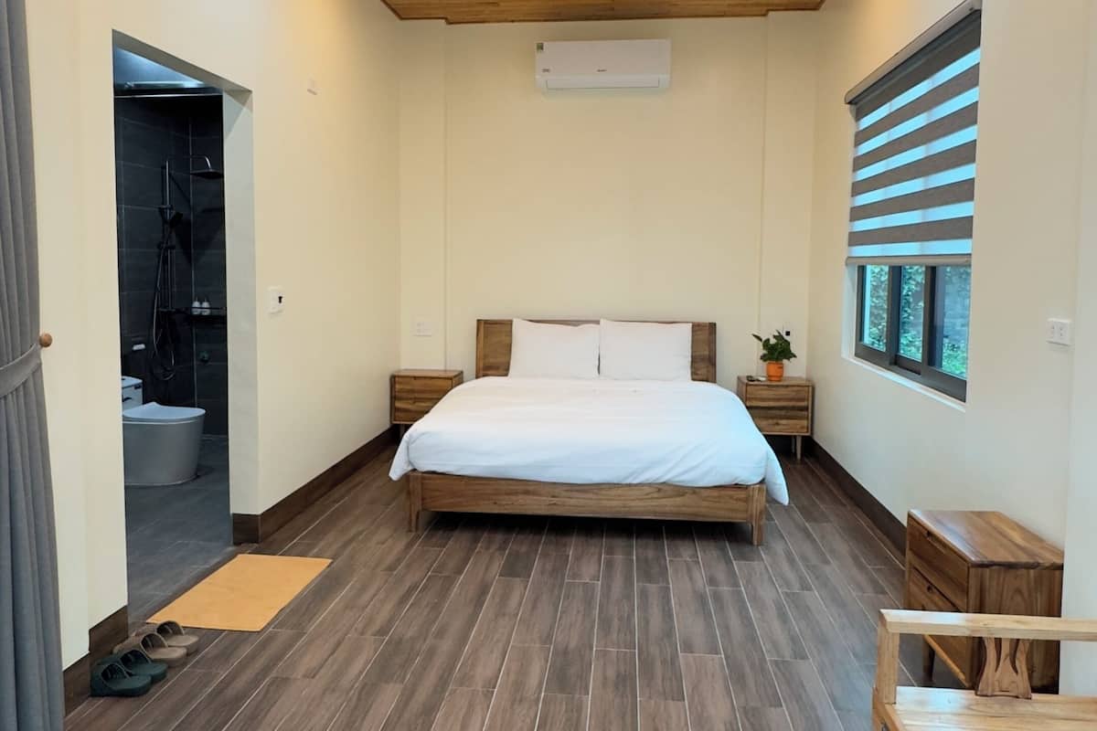 Un dormitorio con techo de madera, una cama grande, una mesita de noche y una puerta que da a un baño.