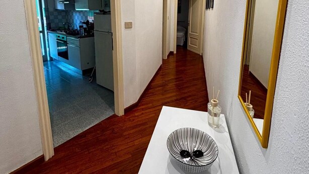Un couloir avec une console blanche, un grand miroir et un plancher en bois.