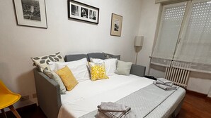 Un lit bien fait, avec des oreillers et une serviette pliée, une table de chevet, une chaise et des tableaux encadrés au mur.