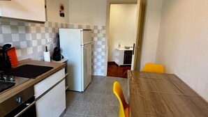 Une cuisine compacte équipée d’un réfrigérateur, d’une cuisinière et d’un évier. On y trouve une table à manger avec des chaises et un petit îlot de cuisine.